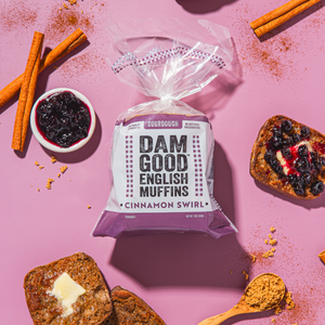 Bag of Dam Good English Muffins with cinnamon swirl on a pink background with muffins and jam.