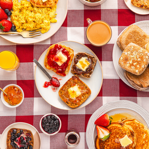 Breakfast table with plates of toast, eggs, and beverages on a red and white checkered tablecloth.