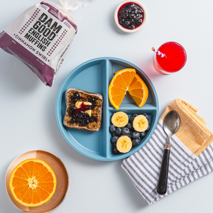 Breakfast setting with a blue plate of toast, fruit, and juice, and Dam Good English Muffins.