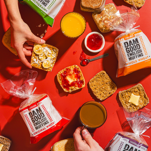 Assorted English muffins with various toppings on a red surface, featuring 'Dam Good English Muffins' packaging.