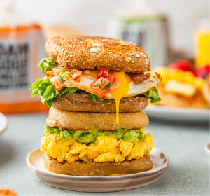 Stacked English muffin breakfast sandwiches with egg and avocado on a plate with a blurred background