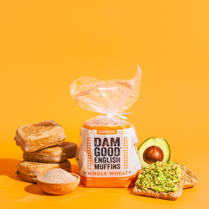 Packaged Whole Wheat English muffins with a sliced avocado on toast against an orange background